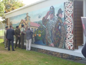 The Trentham Mural is a salute to the past.  IN commemoration of the soldiers who have served  and will serve in the military and their families. Also the community and the role the military plays in it.  I had the pleasure of working alongside NZ defense force artist Captain Matt Gauldie in the creation and installation of this 11m mural.  Although Trentham began as an Army Camp it includes the Army, Navy and Air force who are now combined to make up today the NZ Defence Force.    The different parts of the mural tell the story Trentham has played in NZ history. The Mural reads form left to right, Past to the future.    Out in front, free standing, is soldier on horse back. Horses played a major part in Trentham history in WW1 and were one of Trenthams contributions, to Gallipoli in particular. They marched from Upper Hutt into Wellington and then were shipped of the other side of the world, many never to return. As you follow the mural along you will see more soldiers and guns from this era, also the tents, Trentham was a “Tent city” at this time. A new and under developed camp   Central in the mural is The Clock tower a building which was standing then and still is today, one of the oldest buildings on the camp. In front of this is a young WW2 soldier and his family who are fairwelling him. The proud father, star stuck little brother in Navy clothes and worried mother and sister.   Moving on and into current times is a LAV (not a tank  I have been told many times there is a difference ) Light Armored Vehicle. Above is a helicopter.   Finishing with a modern day soldier who looks to the left and salutes those who played a part in the story before him and a modern day female soldier looking right to the future of the camp. 